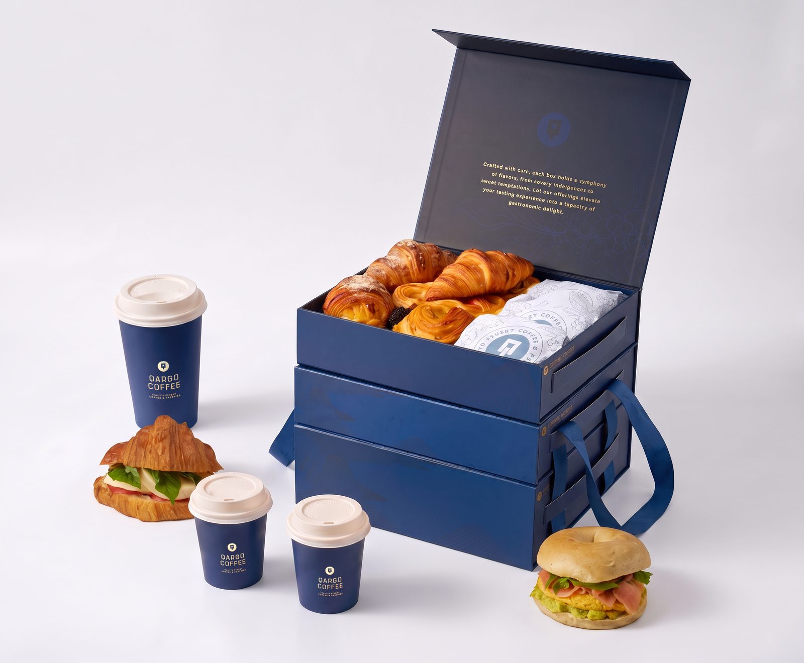 Qargo Coffee catering box stacked and open, croissants inside, with a croissant sandwich, a bagel sandwich and three coffee cups
